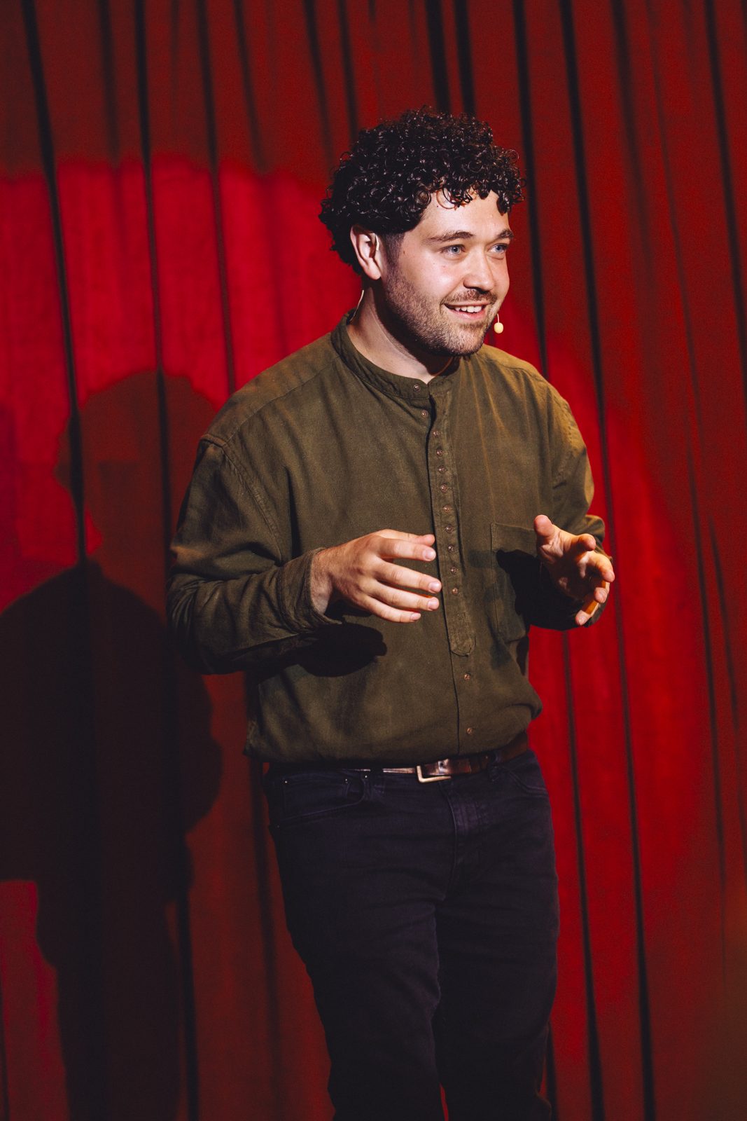 John Stessel mid-performance on stage against a red curtain at Moxy Chelsea