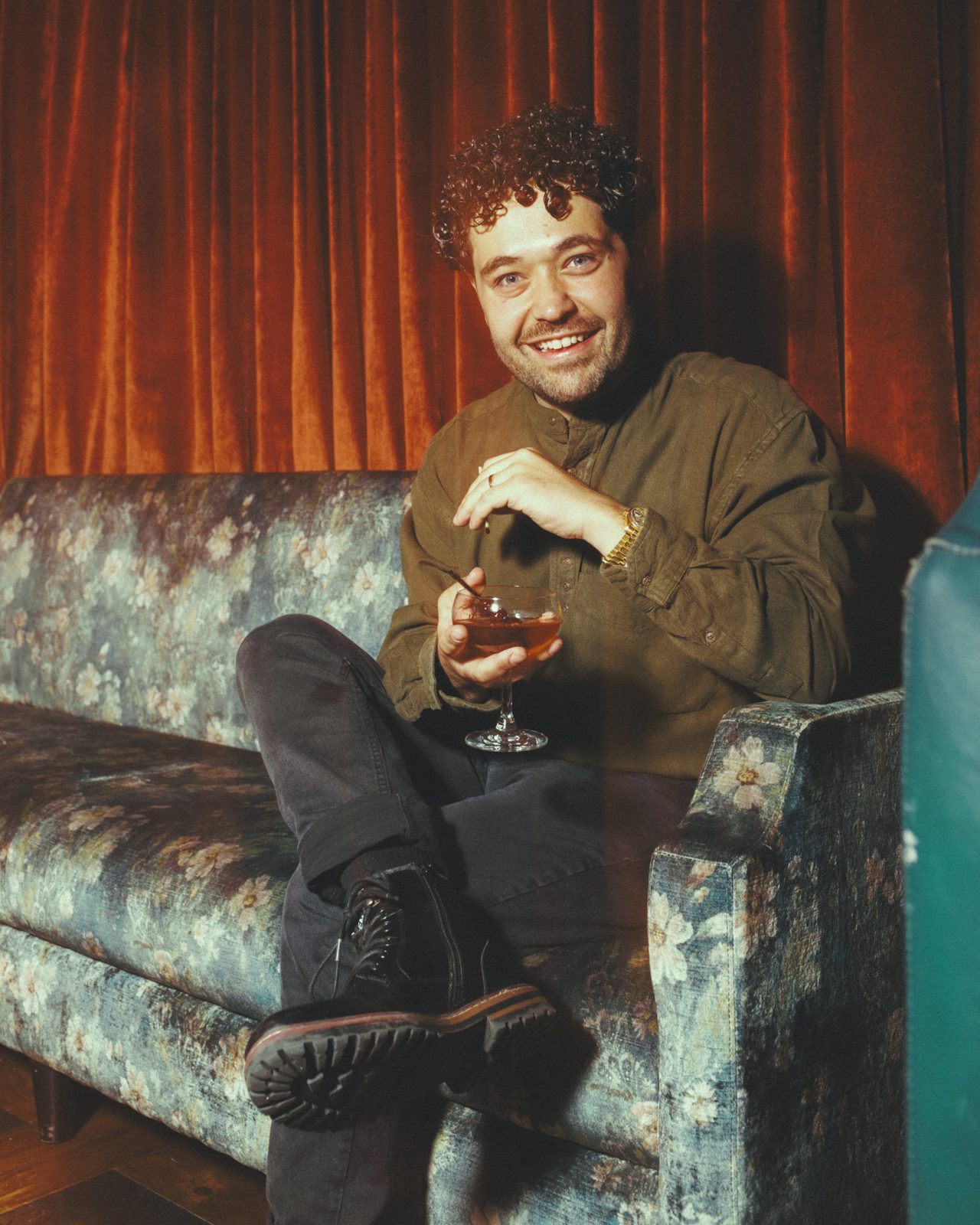 John Stessel smiling on a velvet sofa with a cocktail after a Moxy Chelsea show
